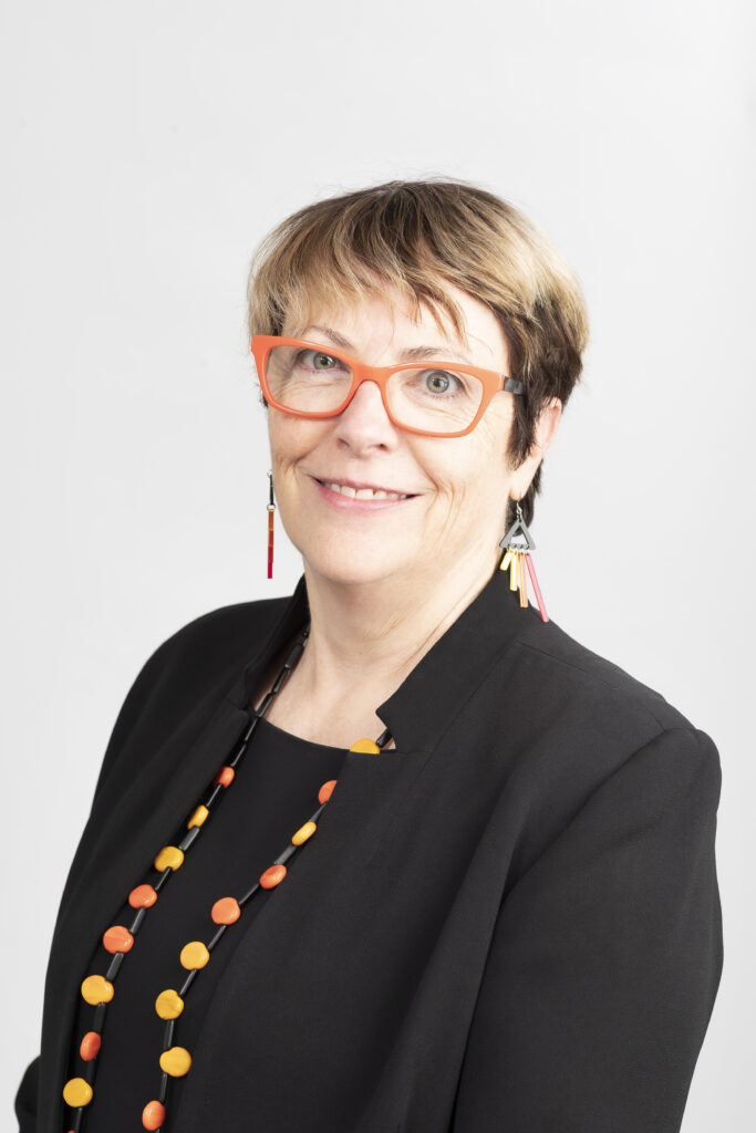 A smiling woman wearing orange glasses, a black dress and a necklace made of beads.