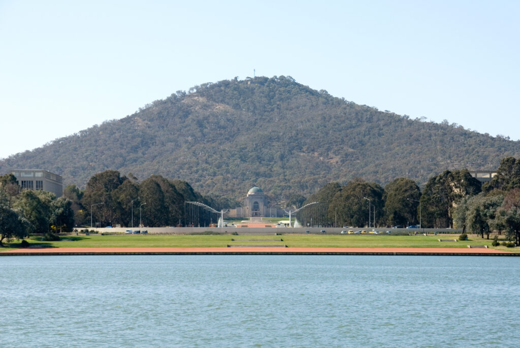 A mountain is in the background, in front of it are a building and a large lake.