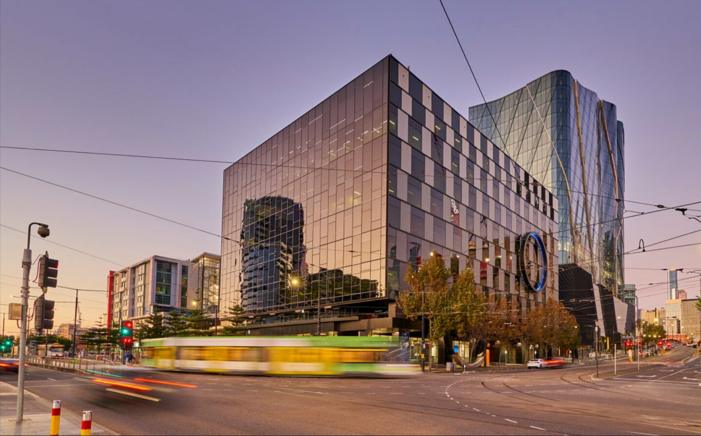 A tall glass building on the corner of a busy street. A tram is speeding by